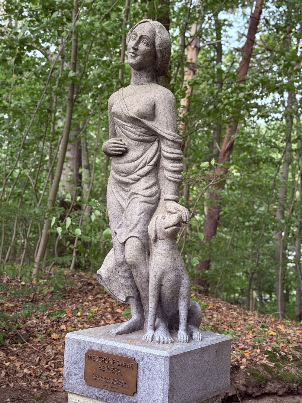 Die Steinfigur der schönen Sabine mit Bronzetafel am Sockel, im Wald