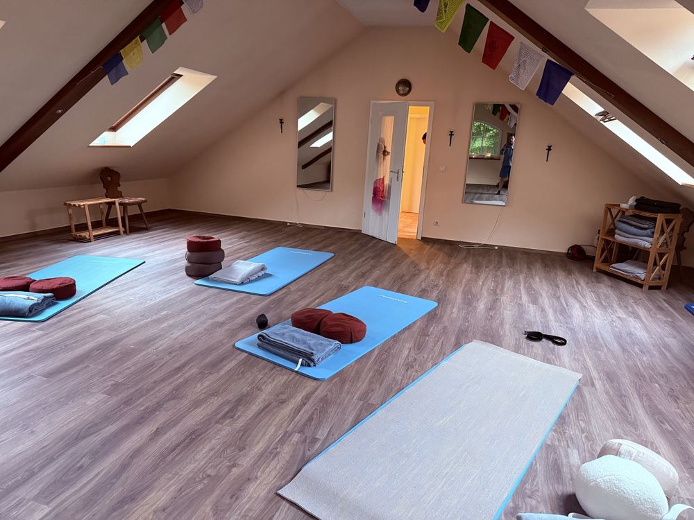 Der helle Yoga-Raum im Dachgeschoss mit Matten, Kissen und Gebetsfahnen
